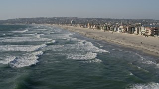 4K aerial stock footage of flying low over waves rolling toward beach and homes, Mission Beach, California Aerial Stock Footage | DCA08_231E