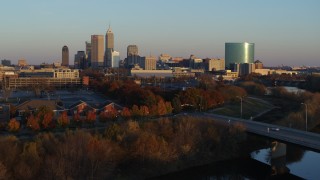 5.7K aerial stock footage of the city's skyline at sunset seen from White River, ascend over bridge, Downtown Indianapolis, Indiana Aerial Stock Footage | DX0001_002925