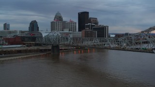 DX0001_003071 - 5.7K aerial stock footage of flying by bridge and and ascend near the arena and city skyline at sunset, Downtown Louisville, Kentucky