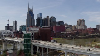 DX0002_117_025 - 5.7K aerial stock footage descend by pedestrian bridge with view of city's skyline, Downtown Nashville, Tennessee