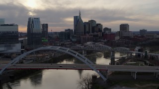 5.7K aerial stock footage ascend past bridge on Cumberland River at sunset, skyline in background, Downtown Nashville, Tennessee Aerial Stock Footage | DX0002_119_045