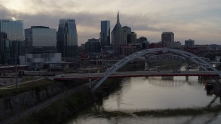 5.7K aerial stock footage the city skyline behind a bridge on Cumberland River at sunset, Downtown Nashville, Tennessee Aerial Stock Footage | DX0002_119_047