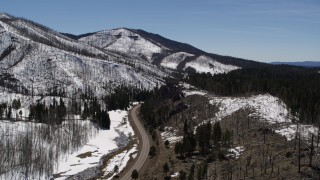 DX0002_134_031 - 5.7K aerial stock footage reverse view of black car on winding road between snowy mountains and evergreens, New Mexico