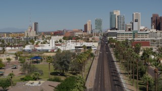 DX0002_137_038 - 5.7K aerial stock footage flyby palm trees at city park and street leading to tall office buildings in Downtown Phoenix, Arizona