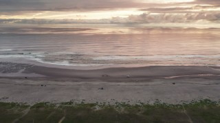 DX0002_148_026 - 4K aerial stock footage of flying away from beach and ocean waves, tilt to focus on clouds at sunset in Long Beach, Washington