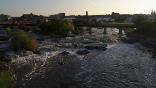 DX0002_176_020 - 5.7K aerial stock footage reverse view of train crossing bridge near waterfalls at sunset in Sioux Falls, South Dakota