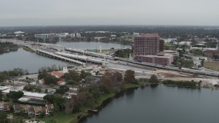 5.7K aerial stock footage of flying away from light freeway traffic and office building by a lake in Orlando, Florida Aerial Stock Footage | DX0003_233_028