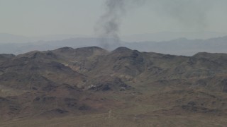 4K aerial stock footage of a column of black smoke rising behind Mojave Desert mountains in San Bernardino County, California Aerial Stock Footage | FG0001_000056