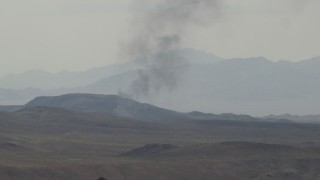 FG0001_000058 - 4K aerial stock footage zoom on black smoke rising behind Mojave Desert mountains in San Bernardino County, California