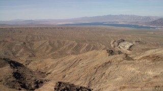 4K aerial stock footage pan across desert hills and approach a scarred hill, with Lake Mead in the background, Nevada Desert Aerial Stock Footage | FG0001_000263